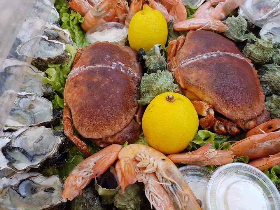 Abondant plateau de fruits de mer : deux tourteaux, des huîtres ouvertes, des crevettes roses, citrons et bulots, servis sur salade.