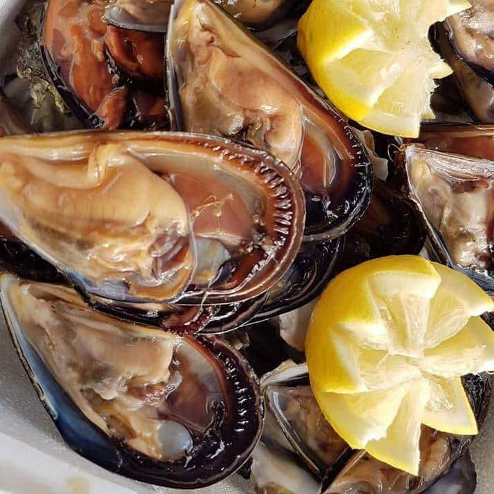 Gros plan appétissant de moules ouvertes dans leurs coquilles brillantes, prêtes à être dégustées avec des quartiers de citron frais.